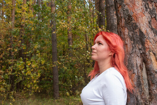 Mid adult 44 years old woman in profile leaning on tree in autumn forest