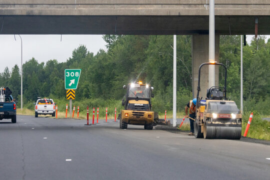 Quebec, Canada, 30 July 2026 : Construction workers operate heavy machinery including a Caterpillar loader and Dynapac roller on a highway underpass.