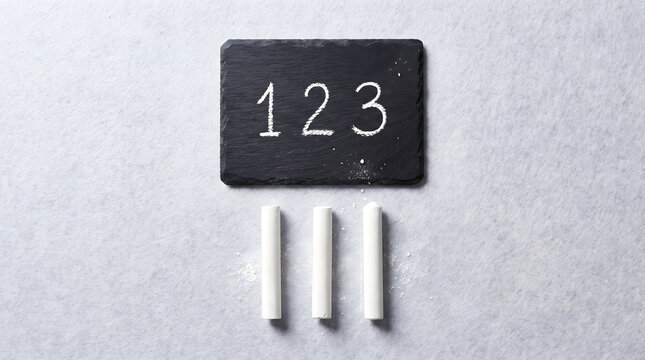A 1 2 3 chalk concept with three white chalk sticks arranged beneath a slate board showing the numbers one two three