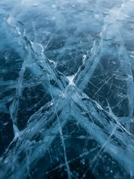 Close up of abstract frozen ice texture featuring deep cracks and fine scratches on blue surface