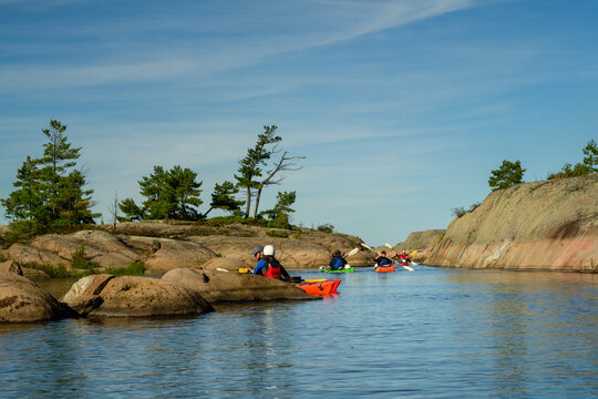Group of sea kayakers paddles through a narrow granite channel between pine-topped islands with copy space on Georgian Bay, Ontario, Canada