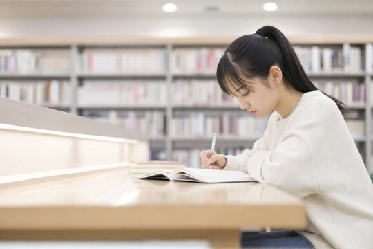 図書館でノートに書き込んで勉強する若い女性