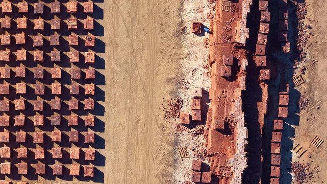 Single laborer moves through geometric stacks of fired clay bricks in Africa