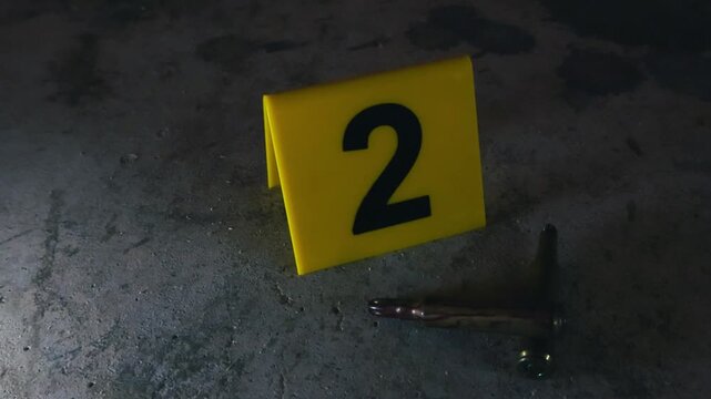Close up of a high caliber bullet shell next to a yellow evidence marker on a dusty concrete floor, representing a concept of forensic investigation and criminal evidence gathering