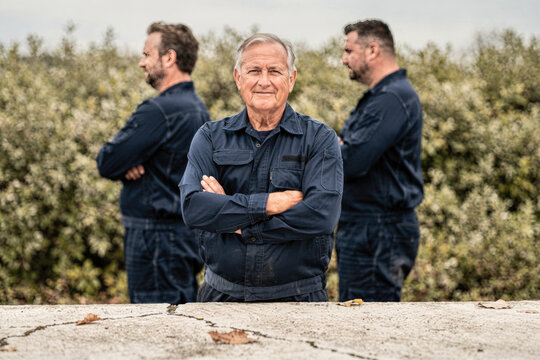 Confident Senior Man in Workwear with Team in Background