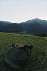 Fototapeta premium Backpack on a meadow with distant mountains, conveying outdoor travel, landscape, solitude, and a moment of quiet adventure in nature.