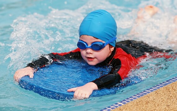 Child swimming in pool with kickboard and goggles, swim lesson training, front view close-up