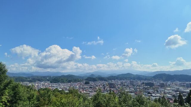 Beautiful panoramic view of Takayama cityscape and distant Northern Alps mountain range under a clear blue sky with fluffy clouds from Sky Park in Gifu, Japan. Perfect for tourism and website headers.