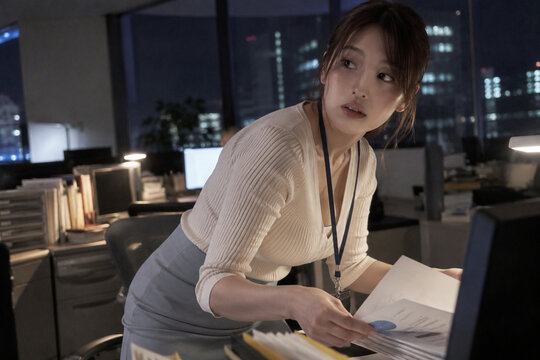 夜の机でグラフ入り資料を扱う白いカーディガンの女性