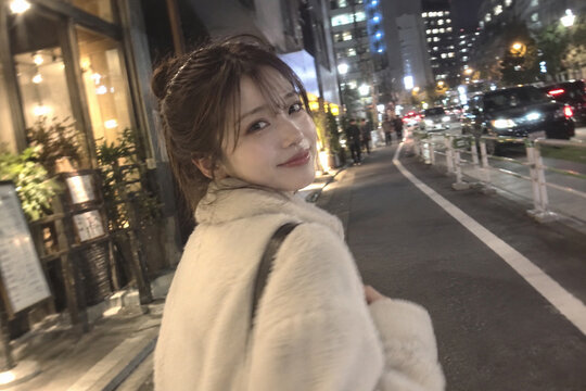 夜の車道沿いで振り返るクリーム色のボアコートの女性