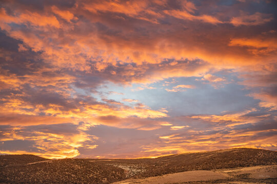 Fiery orange sunrise clouds spreading over dark rolling prairie hills at dawn