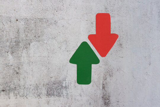 Upward green arrow and downward red arrow on weathered surface