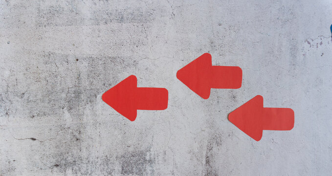 Concrete wall with three bright red arrow symbols pointing left