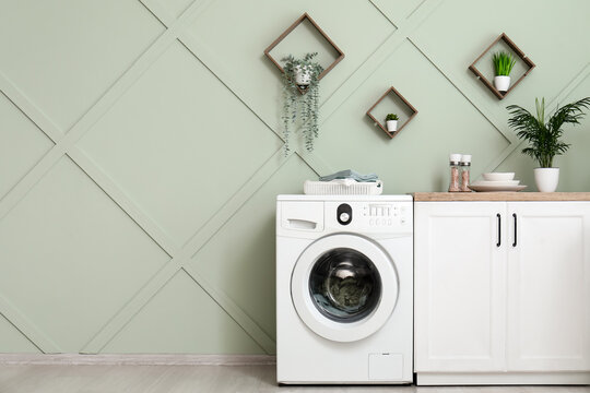 Home laundry and interior design, modern washing machine in a stylish kitchen with green wall paneling and house plants for domestic lifestyle