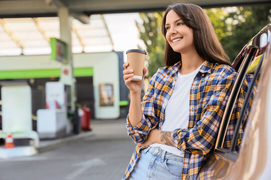 Road trip travel and coffee break, happy woman holding a paper cup while leaning on her car at a gas station during a summer vacation journey