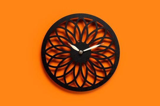 Time management and productivity concept, black decorative wall clock with geometric floral pattern on a bright orange background