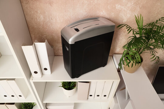 Shredder with folders and plant on shelf in office