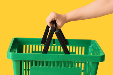Obraz premium Female hand with green shopping basket on yellow background
