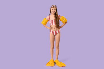 Cute little girl in swimsuit with inflatable armbands and flippers on purple background © Pixel-Shot