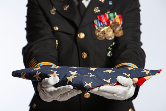 Military Officer in Dress Uniform Holding Folded American Flag with Medals