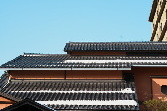 島根県大田市温泉津の青空の下で雪が線状に残る黒瓦の重なる屋根と赤茶の壁
