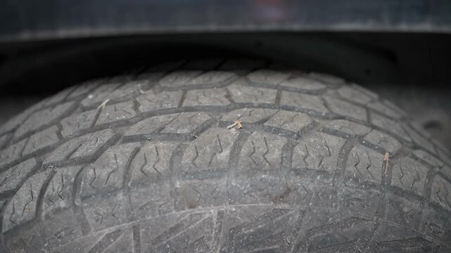 A close-up shot of an all-terrain car tire tread with noticeable wear and small cracks, positioned underneath a vehicle fender.