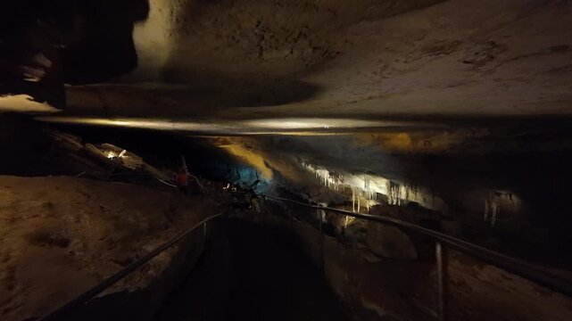 People walking on path in illuminated cave with stalactites.
