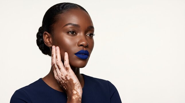 Confident black woman with vitiligo on hand wearing bold blue lipstick in studio portrait