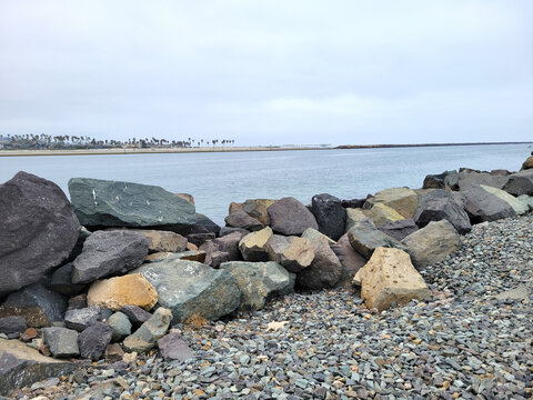 Scenic view of Mission Bay Entrance Channel in San Diego featuring large riprap jetty boulders and a distant shoreline.
