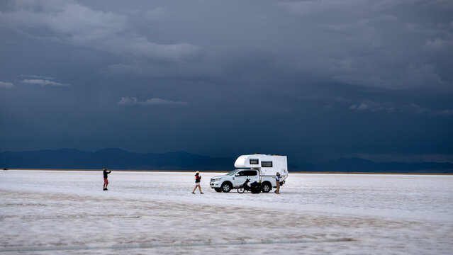 Viajeros explorando un inmenso salar en camper 4x4 bajo un cielo tormentoso.   