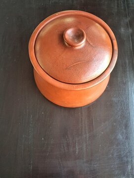 Traditional terracotta clay pot with lid on dark wooden surface for rustic culinary background.