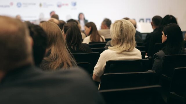 Business conference audience seated in an event hall and listening to a speaker on stage during a professional seminar, forum or corporate presentation.