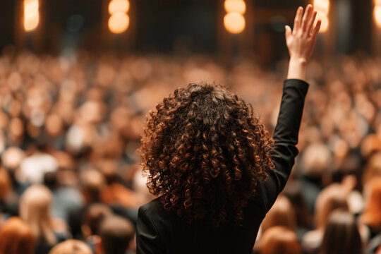Person raising their hand to participate in a large professional business conference