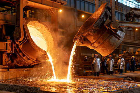 Molten metal pours from large industrial molds. Workers observe the process in protective gear. Bright sparks fly as hot liquid flows into a mold. Heavy metal production in a factory