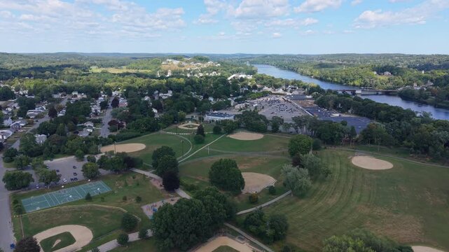 Wide daytime drone fly-over of urban Haverhill green park with baseball diamonds and nearby Merrimack River border near the residential neighborhood, Massachusetts, US