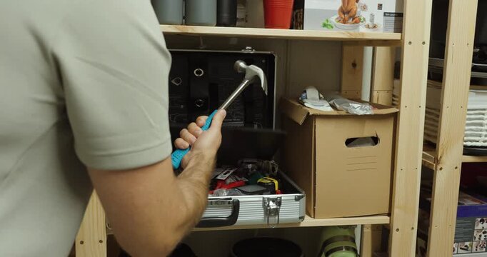 Person searches through a toolbox, finds a hammer and takes it out for use.