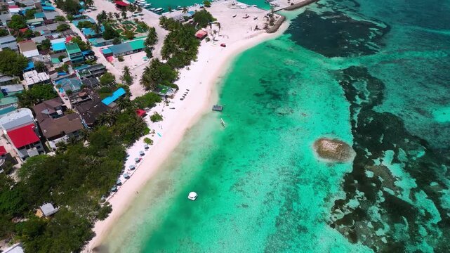 High angle drone perspective of local island town and white beach bordering vibrant coral reef sea. Ideal visual asset for travel guides, destination, and holiday videos.Himmafushi.Maldives