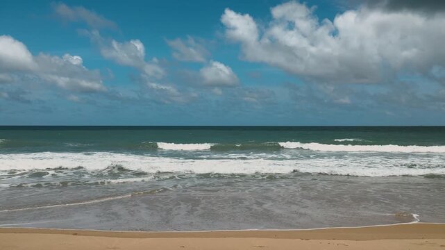 Tropical Sandy Beach with Ocean Waves Under a Blue Sky and White Clouds in Thailand