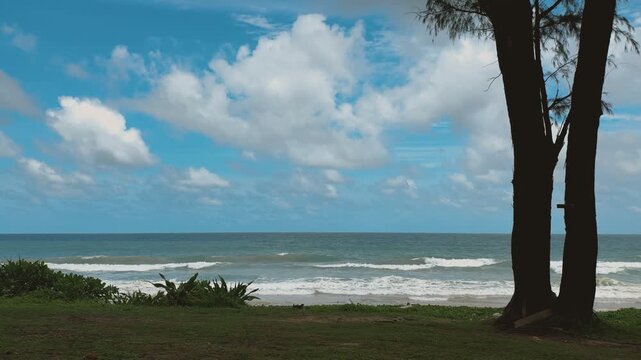 Idyllic tropical beach scene in Thailand with ocean waves, blue sky, and a prominent tree.