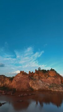 Scenic Landscape of Red Rock Formations and Calm Lake Under Blue Sky in Thailand
