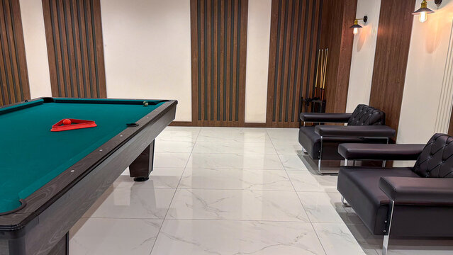 Modern indoor recreation room with billiard table, pool cues and comfortable armchairs in a contemporary residential complex.