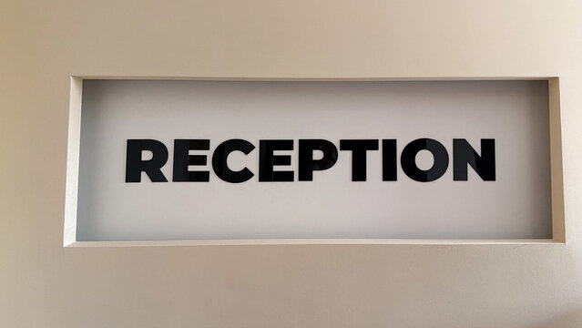 Reception sign with black lettering on a minimalist white wall in a modern hotel, apartment complex or office building interior.