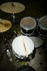Obraz premium Vertical shot of drum kit with drumsticks resting on snare drum outdoors. Musical instrument set ready for live concert performance or indie music promotion