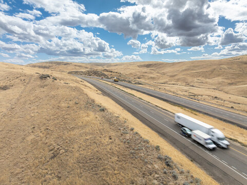 White semi-truck travels alone on desert highway under dramatic sky