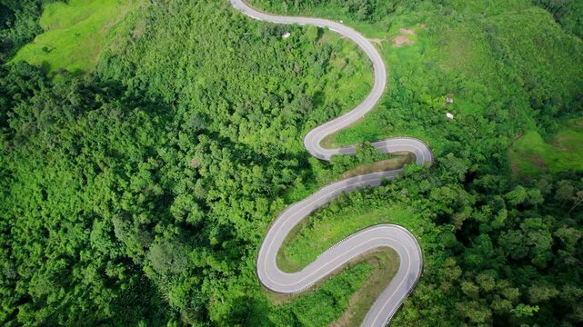 Top view of countryside road passing through the green forrest and mountain