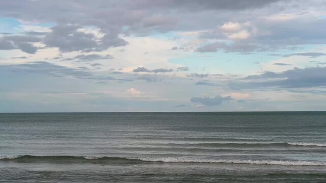 Calm sea and gentle waves under a cloudy sky at the beach.