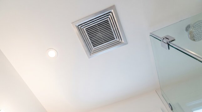A metal air vent installed on a white bathroom ceiling for interior ventilation.