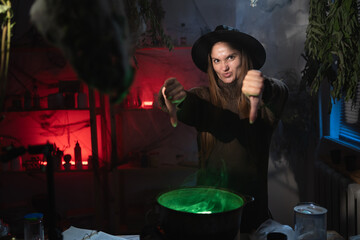 Unhappy realistic witch brewing a potion in cauldron pointing thumbs-down dislikes gesture. Blend of everyday life with traditional witchcraft, magic and mystical atmosphere © Andrii Lysenko