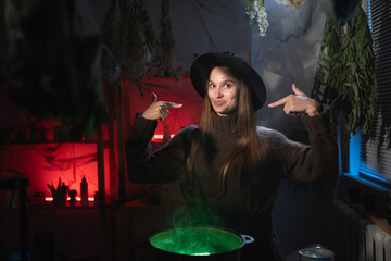 realistic witch brewing a potion in cauldron pointing fingers on her smile and lips. Blend of everyday life with traditional witchcraft, magic and mystical atmosphere © Andrii Lysenko