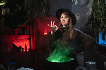 Realistic witch brewing a potion in cauldron showing OK gesture on camera. Blend of everyday life with traditional witchcraft, magic and mystical atmosphere © Andrii Lysenko